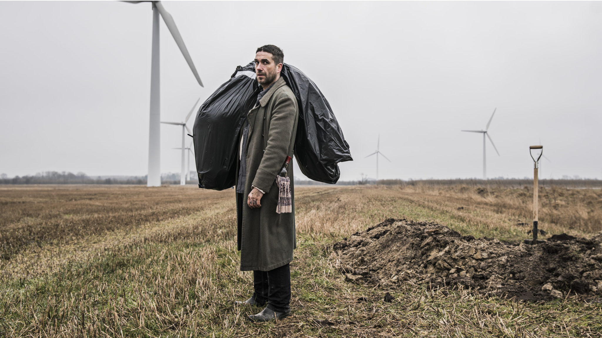 Szenenbild aus „Small Town Killers“: Igor (Marcin Dorocinski) mit einem Leichensack über der Schulter, im Hintergrund ein ausgehobenes Grab.